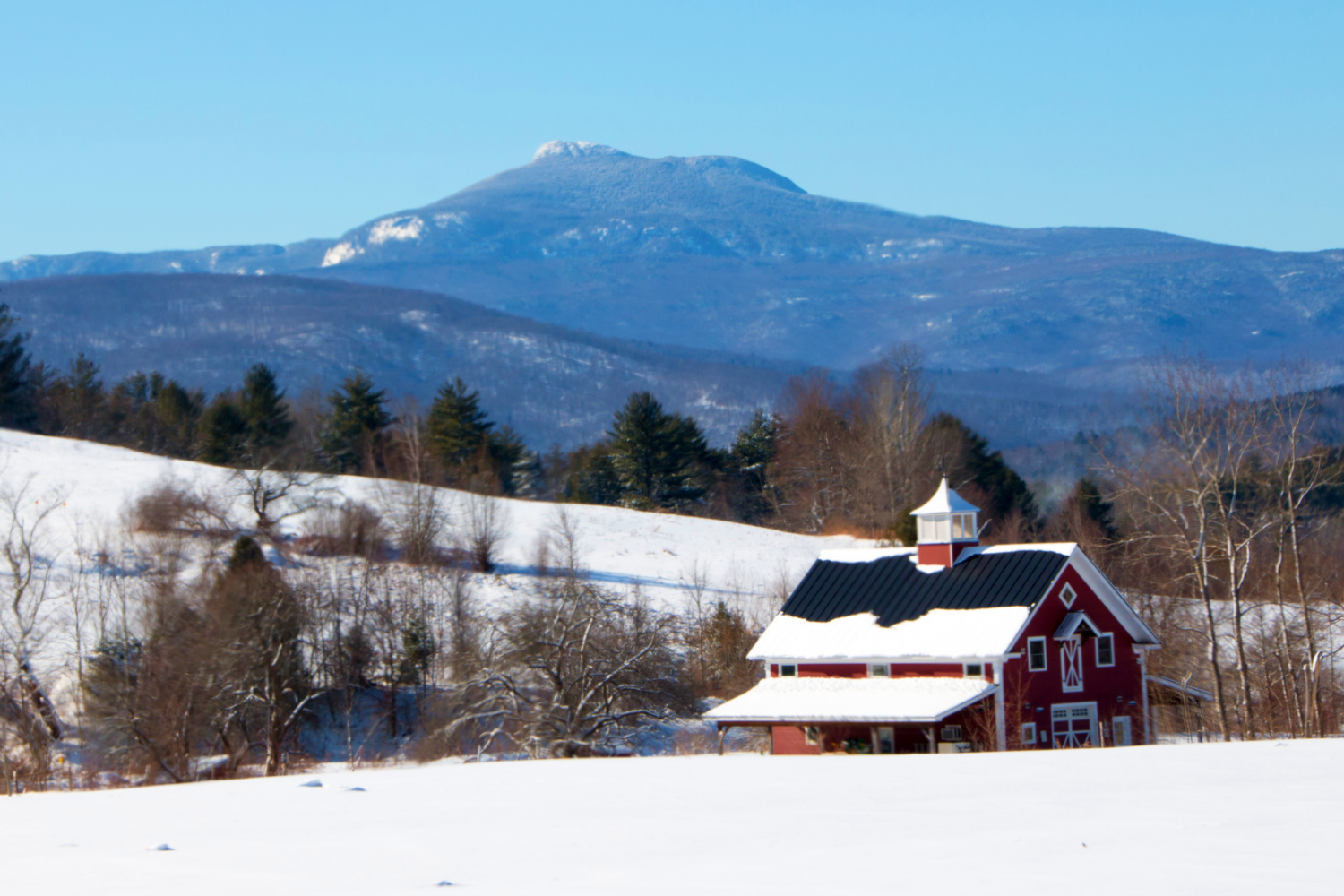 A red barn with snow and Camel's Hump in the background